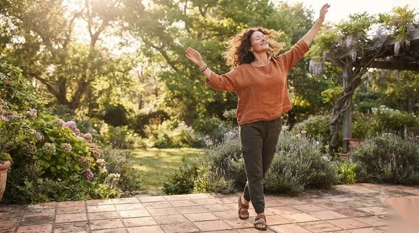 Woman dancing joyfully in a sunlit garden, arms raised